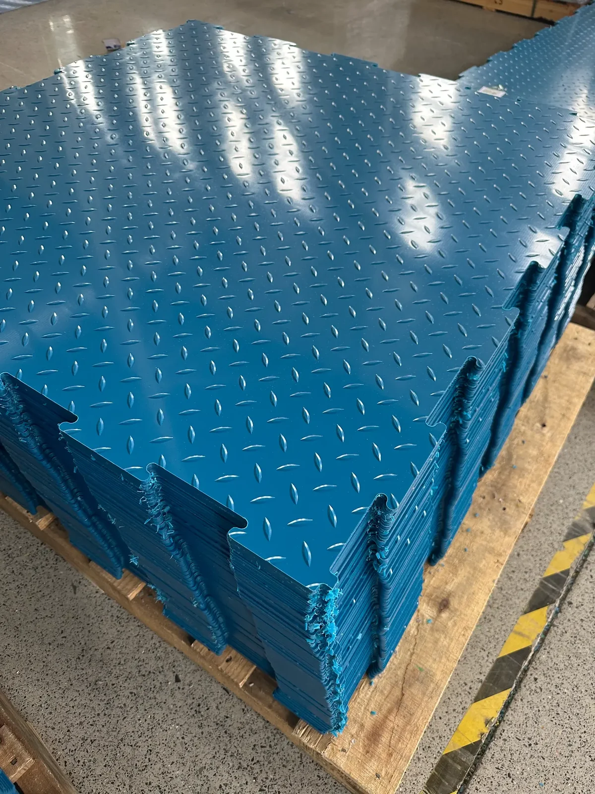 Company-supplied factory photo: blue HDPE interlocking floor panels stacked on a pallet.